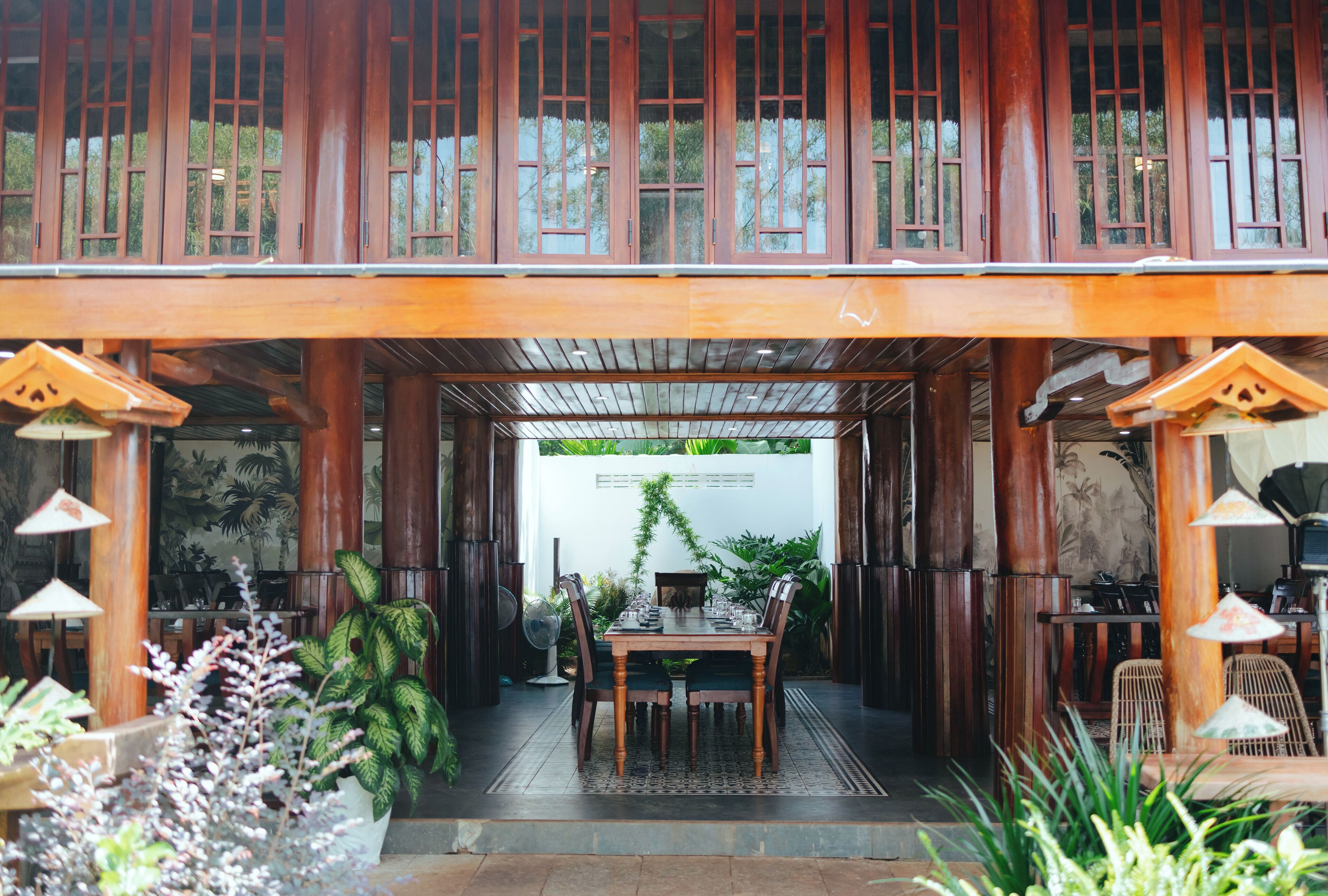 A wooden dining area with a table and chairs, surrounded by potted plants and a view of greenery.