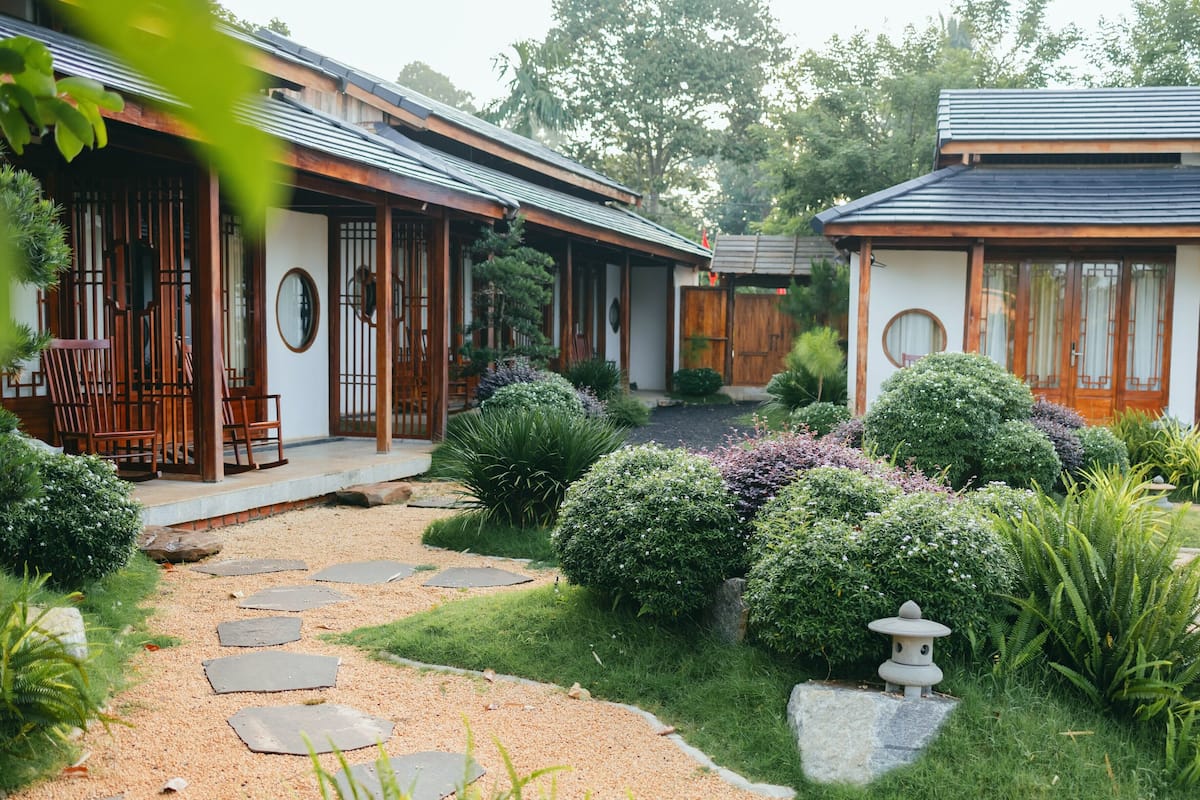 En traditionell japansk trädgård med stenbelagda gångar, välklippta buskar och en liten stenlykta.