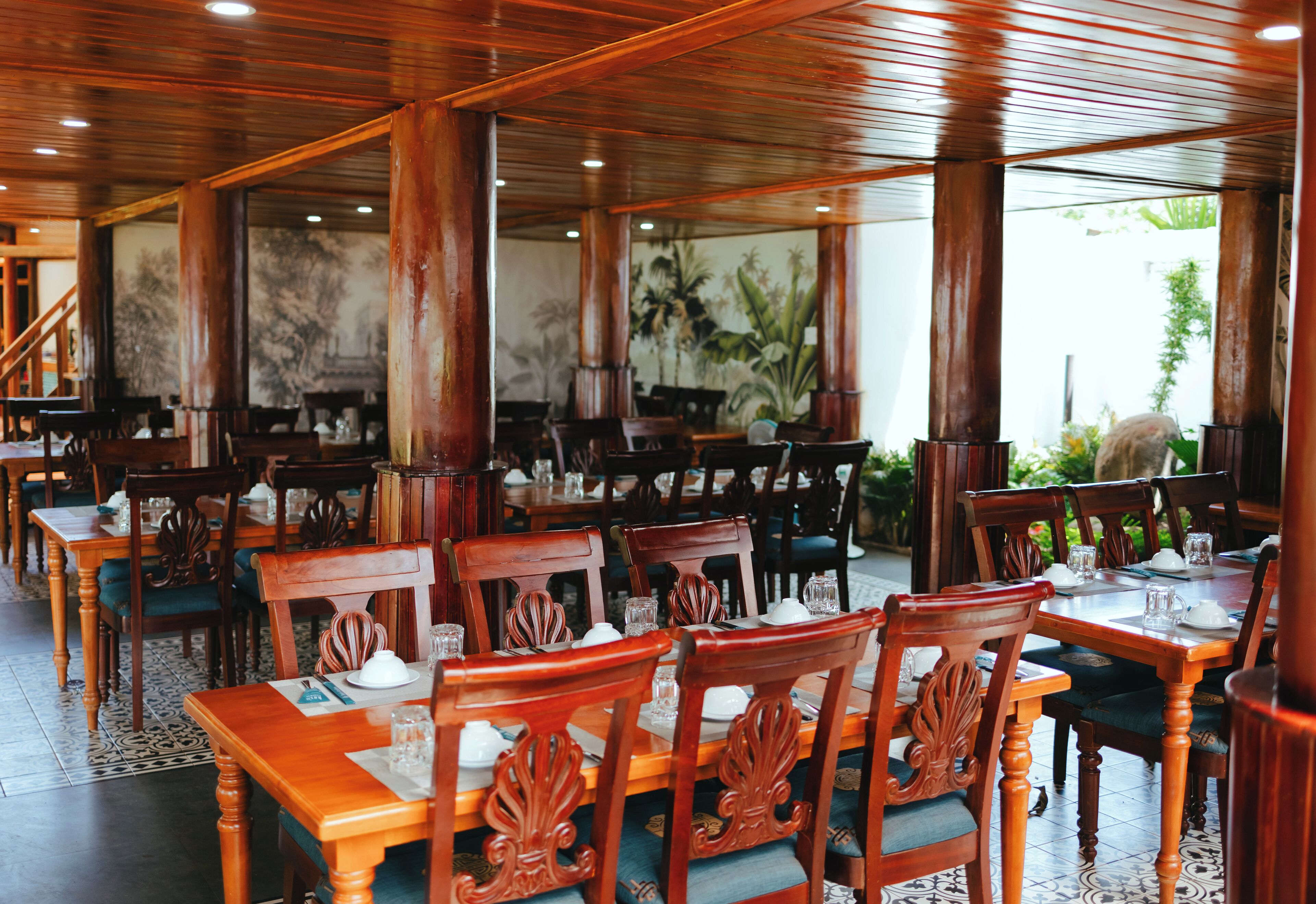 A restaurant with wooden tables and chairs, large windows, and a tiled floor.