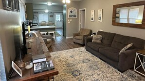 A living room with a brown couch, a coffee table, and a rug. There is a dining area in the background with a table and chairs. - New Kitchen,FirePit,FamFriendly,Sleeps10:LakeLux (Arnolds Park)
