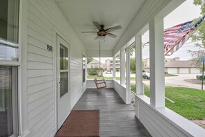 Eine überdachte Veranda mit Deckenventilator, einer Schaukel und Blick auf ein Wohngebiet mit einer amerikanischen Flagge.