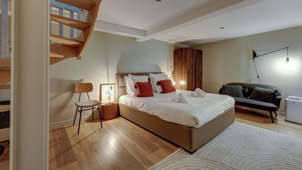 A modern bedroom with a large bed, a wooden staircase, a sofa, and a small table.