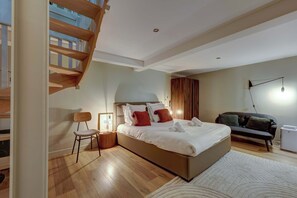 Une chambre moderne avec un grand lit, un escalier en bois, un canapé et une petite table.