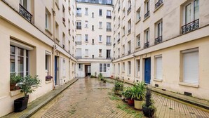A courtyard with a cobblestone floor, potted plants, and buildings with balconies and windows.