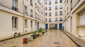 A courtyard with a cobblestone floor, potted plants, and a blue door at the far end.