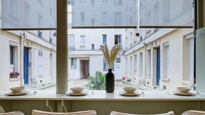 A dining area with a view of a courtyard, featuring a table set with plates, glasses, and a vase.