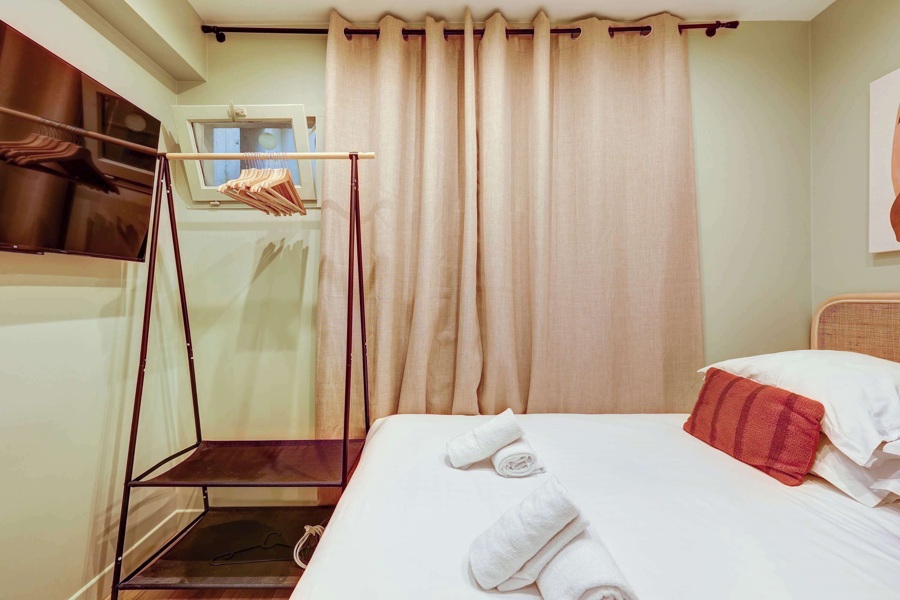 Habitación de hotel con cama, ventana, cortina y perchero.