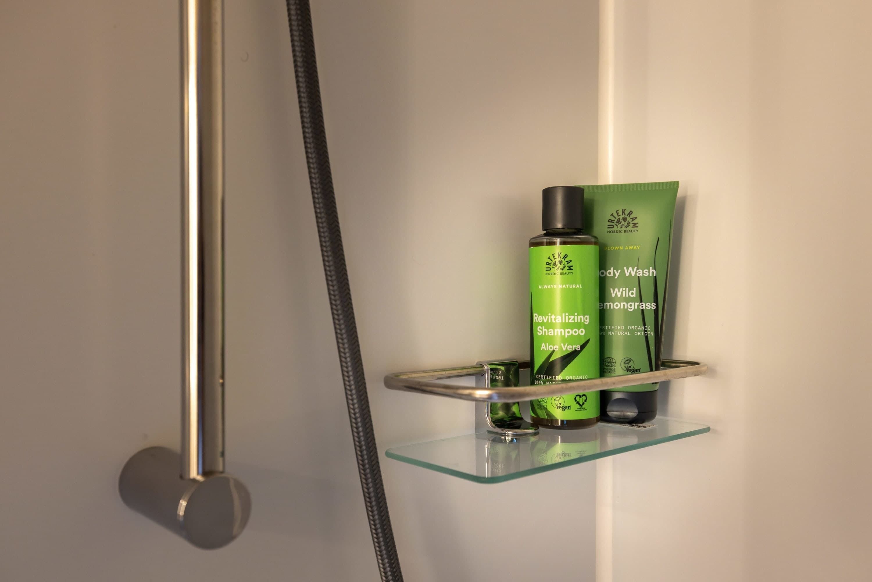 Area doccia con ripiano in vetro che contiene una bottiglia di shampoo e un flacone di bagnoschiuma.