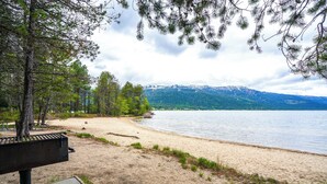 Vista de un lago con una playa de arena, árboles y montañas al fondo.