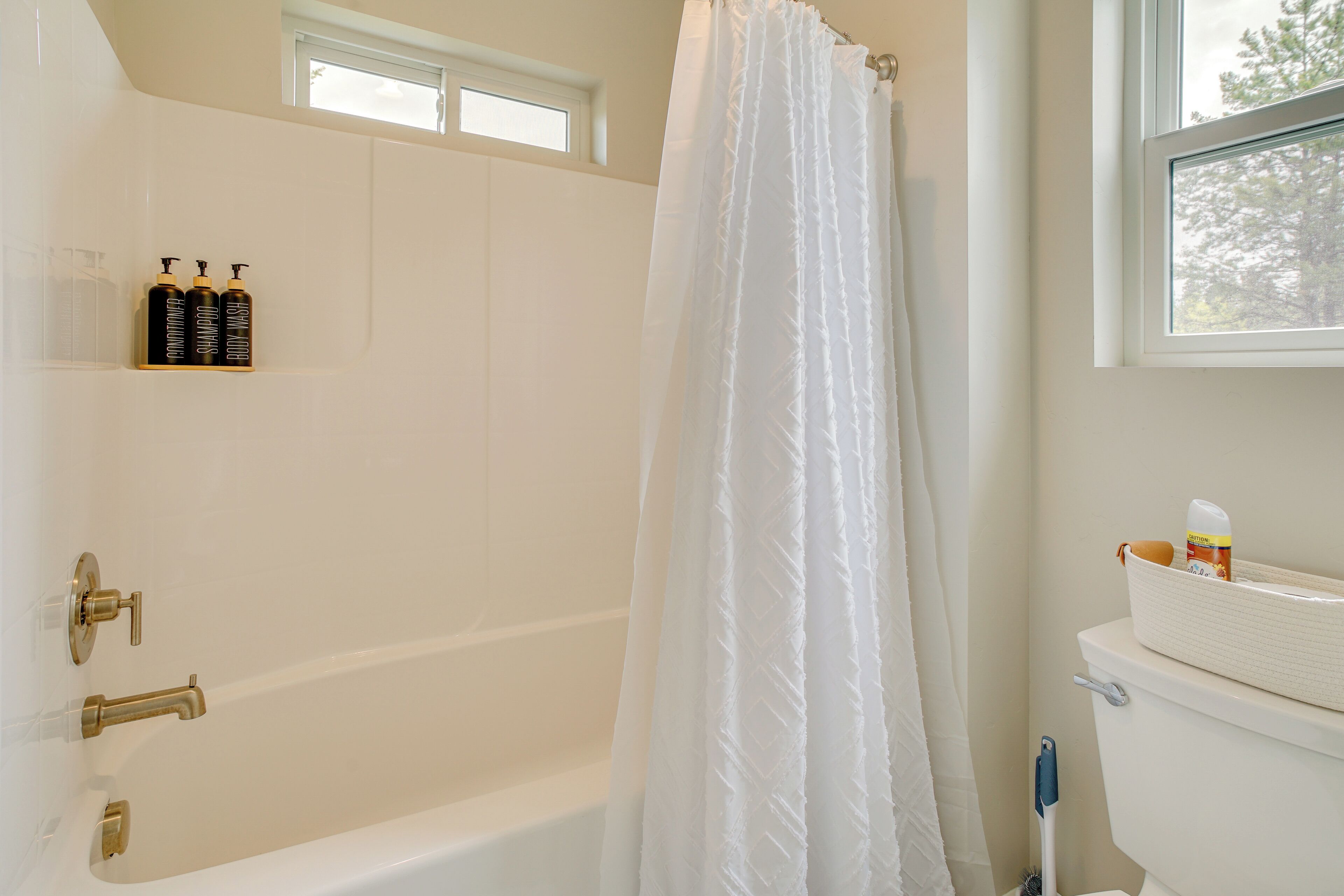 A bathroom with a bathtub, a toilet, and a window. There are toiletries on a shelf.