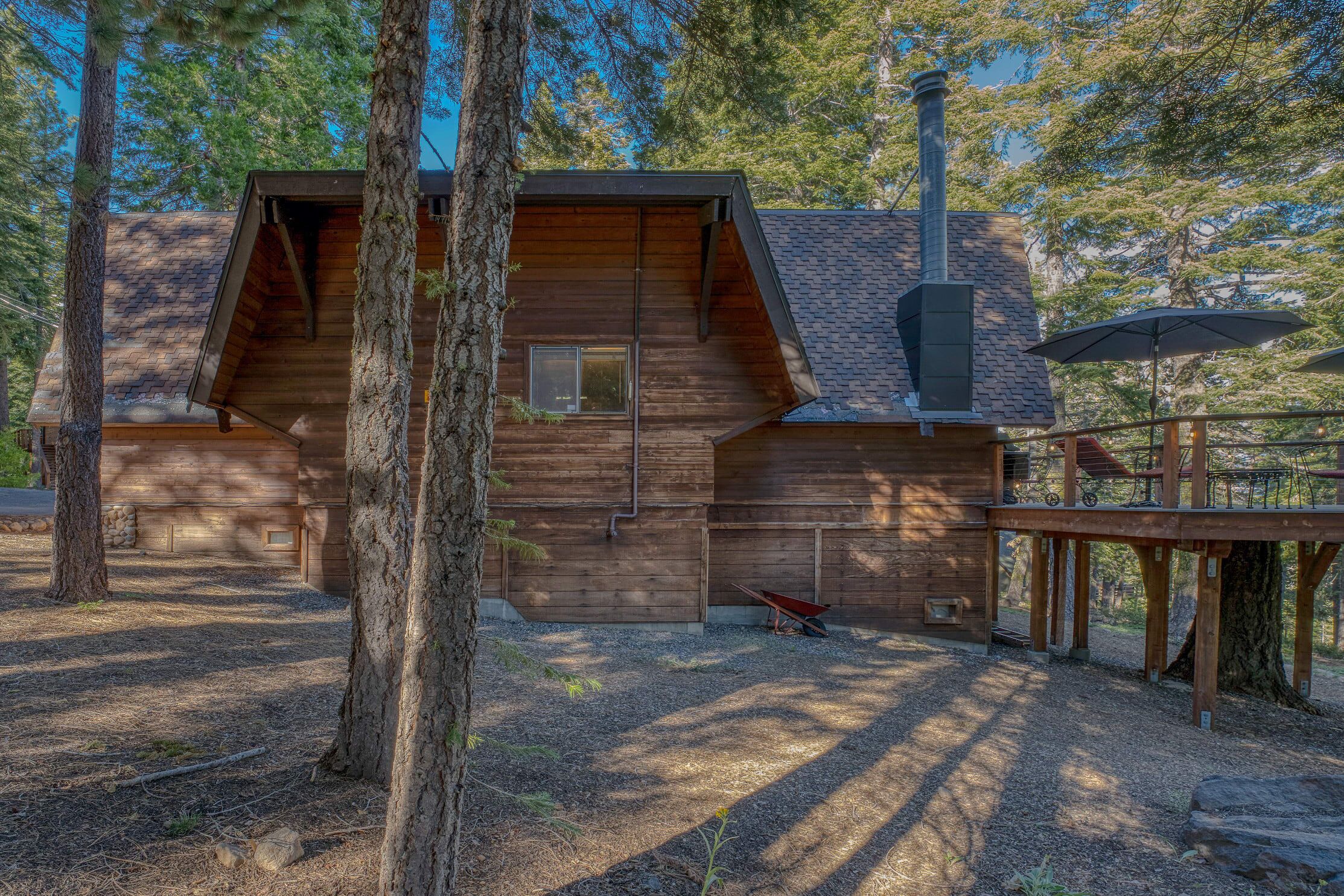 A wooden cabin with a sloped roof, a chimney, and a deck area.