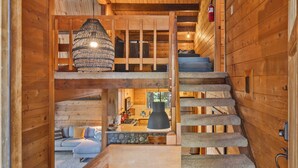 Un intérieur en bois avec un escalier menant à une chambre à coucher située en mezzanine, un coin repas et une cuisine.