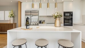 Une cuisine moderne dotée d’un îlot central, d’appareils électroménagers en acier inoxydable, de luminaires suspendus et d’un vase de fleurs.