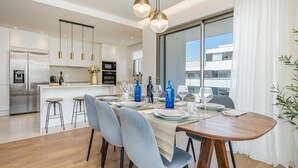 Une cuisine moderne dotée d’un îlot central, d’appareils électroménagers en acier inoxydable et d’un coin repas avec une table en bois et des chaises grises.