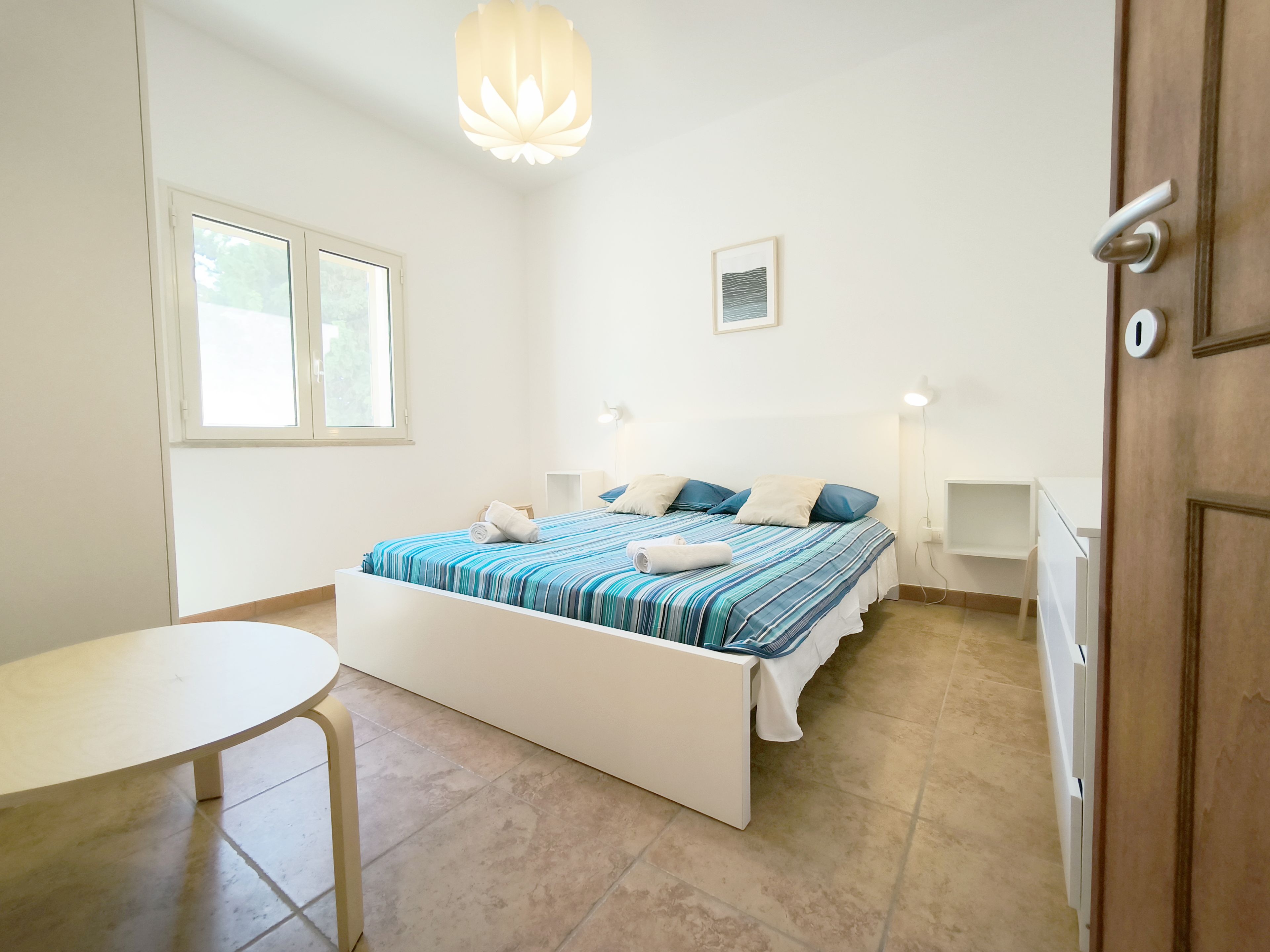 Ein Schlafzimmer mit Bett, Nachttischen, Schreibtisch, Stuhl, Fenster und Tür.