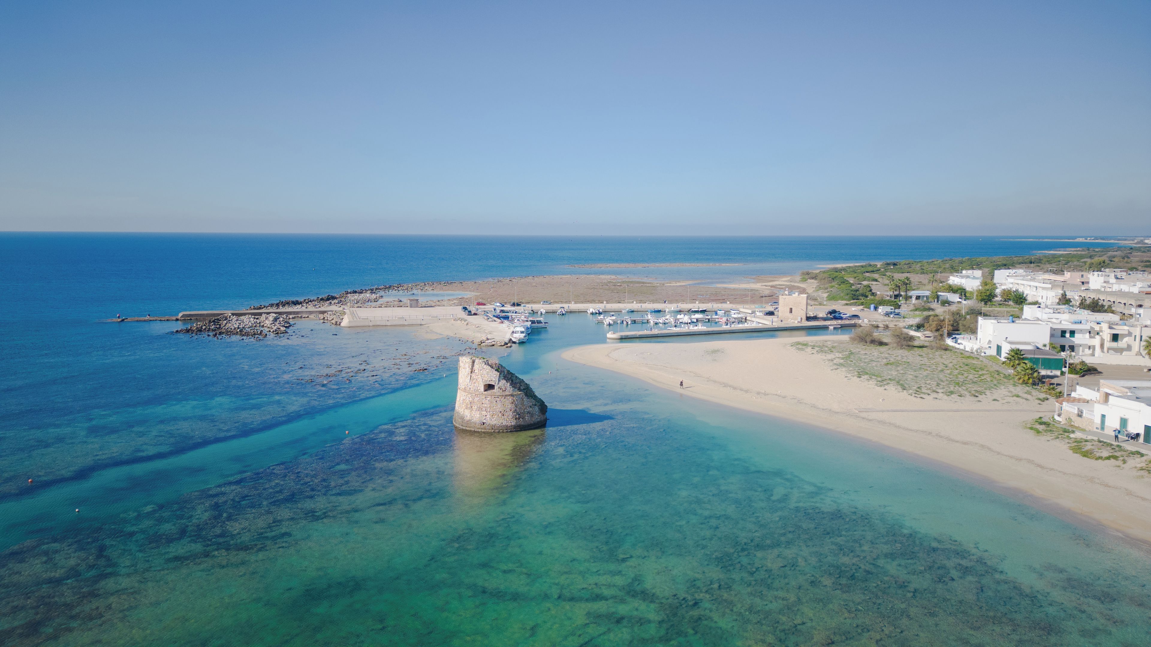 Un pueblo costero con aguas cristalinas, un promontorio rocoso y un puerto deportivo.