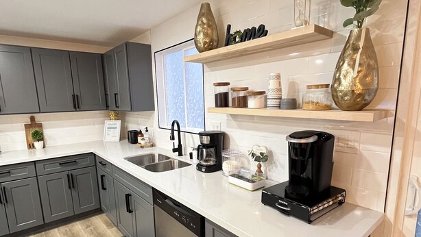 Una cocina moderna con armarios grises, encimera blanca y una cafetera.