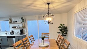 Un comedor con una mesa y sillas de madera, un candelabro y vistas a la cocina al fondo.
