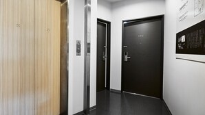 A modern elevator with a wooden panel and a dark door, both featuring a metallic handle. - IZUTSU HOTEL KYOTO KAWARAMACHI SANJO (Kyoto)