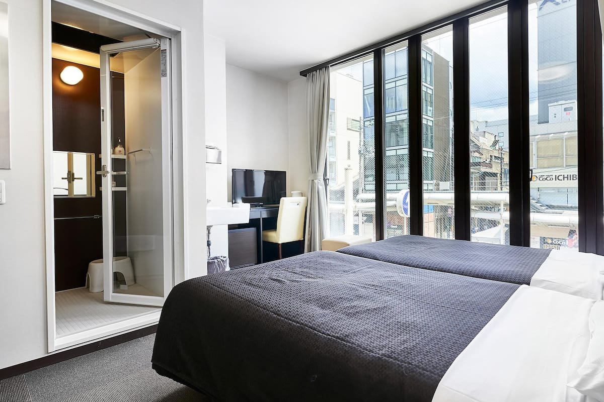 A hotel room with a bed, a desk with a chair, a mirror, and a window with curtains.