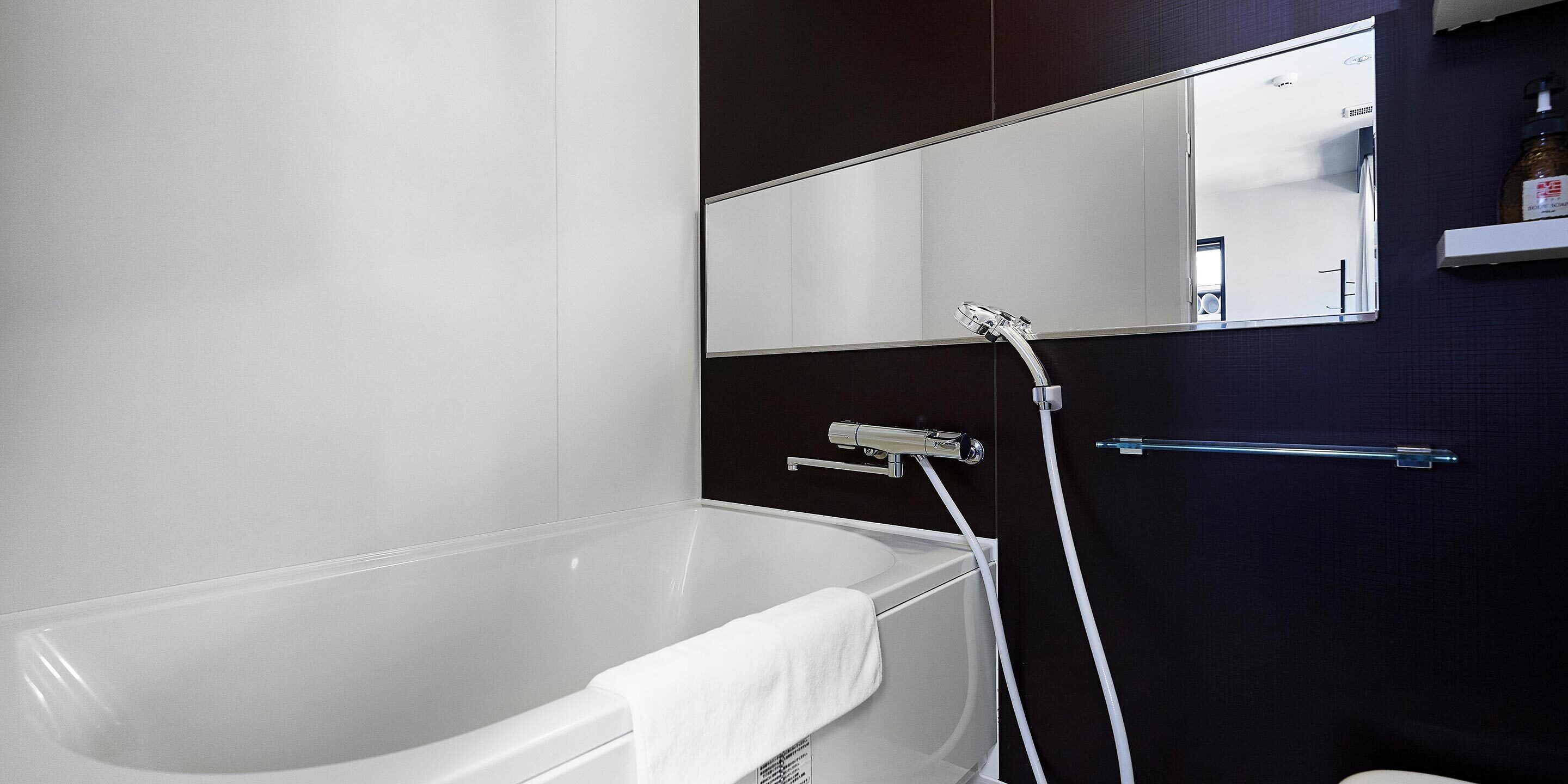 Ein modernes Badezimmer mit einer weißen Badewanne, einem großen Spiegel und einer Duschbrause.