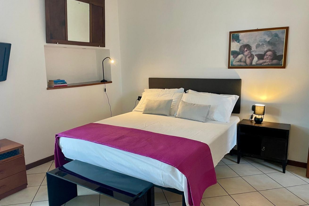 Una cama bien hecha con una colcha blanca y rosa, un cabecero de madera y una mesita de noche con una lámpara.