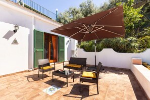 Een terras buiten met rieten meubilair, een grote parasol en een betegelde vloer.