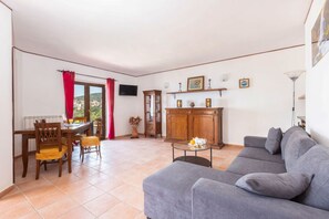 Una sala de estar con un sofá gris, una mesa de comedor con sillas, un aparador y un televisor en la pared.