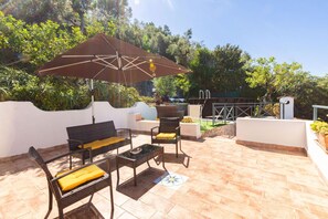 Une terrasse extérieure aménagée avec des meubles en osier, une table et un grand parasol.