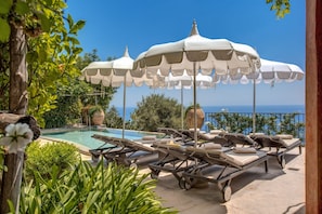 A poolside area with lounge chairs and umbrellas, overlooking a clear blue sky and sea.
