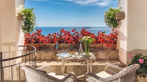 A balcony with wicker furniture, a table with a vase and plates, and hanging flower baskets. - MyExclusiveItaly - Lux Historic Villa with Pool & Amalfi Coast View (Positano)