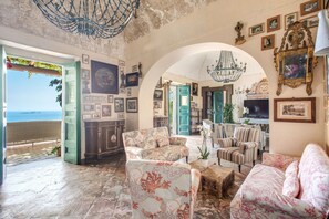 Un salon spacieux avec vue sur la mer, agrémenté d’une grande porte en arc, de plusieurs coins salon et d’une variété de tableaux encadrés qui ornent les murs.