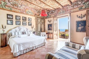Een ruime slaapkamer met een groot bed, een stoel en uitzicht op zee door een open deur.