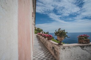 Un balcó amb sòl de rajola, plantes en testos i vista al mar.