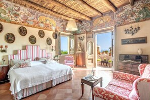 Un dormitorio amplio con una cama grande, una silla y un escritorio. Hay varias fotografías enmarcadas en las paredes y un candelabro.