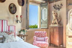 Um quarto com uma cama, uma cadeira, uma janela e uma estátua.