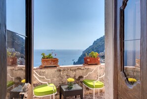 Un balcon avec vue sur la mer, des plantes en pot et deux chaises vertes.