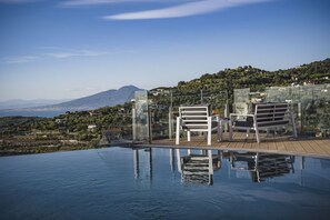 Una piscina infinita con agua cristalina que refleja el entorno, dos sillones blancos y una vista de un paisaje montañoso al fondo.