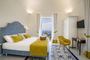 A hotel room with a bed, a chair, a desk, a TV, and a balcony with a view.