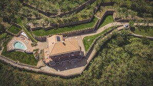 Vista aérea de un complejo turístico con piscina, un edificio grande de techo con tejas y un recinto amurallado.