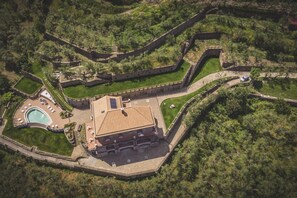 An aerial view of a resort with a swimming pool, a large building with a tiled roof, and a walled enclosure. - MyExclusiveItaly - Villa Breathtaking view near Nerano (Massa Lubrense)