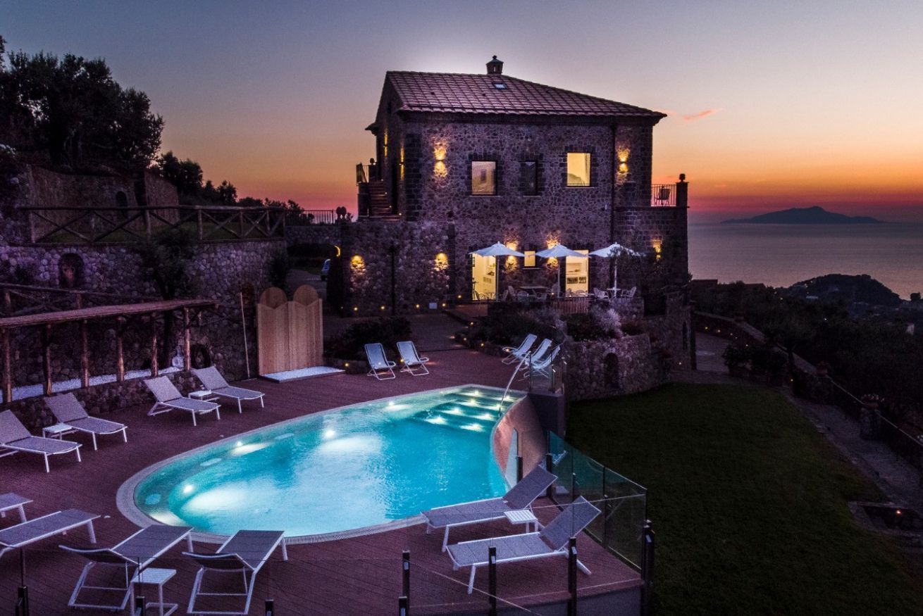 Ein Steinhäuschen mit Swimmingpool, Liegestühlen und Blick auf das Meer bei Sonnenuntergang.