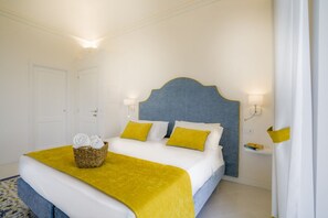 Una habitación de hotel con una cama grande, paredes blancas, un cabecero azul y detalles en amarillo.