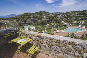 A stone wall with a pool and lounge chairs, overlooking a hillside with houses. - MyExclusiveItaly - Villa Breathtaking view near Nerano (Massa Lubrense)