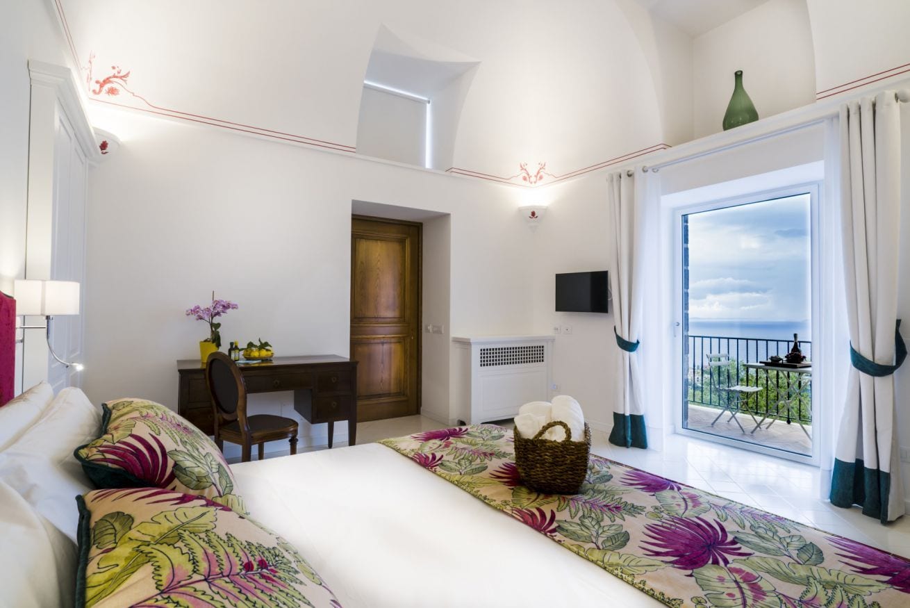 A hotel room with a bed, a desk, a chair, a window with a view, and a balcony.