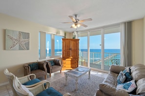 Relax in this spacious living area with a high ceiling and ceiling fan, featuring a large sliding glass door leading to a balcony with ocean views and a pier.