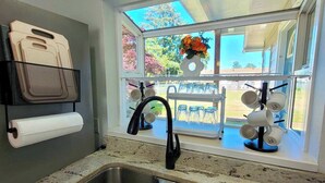 Una cocina con un lavamanos doble, una ventana con un arreglo floral y un dispensador de toallas de papel.