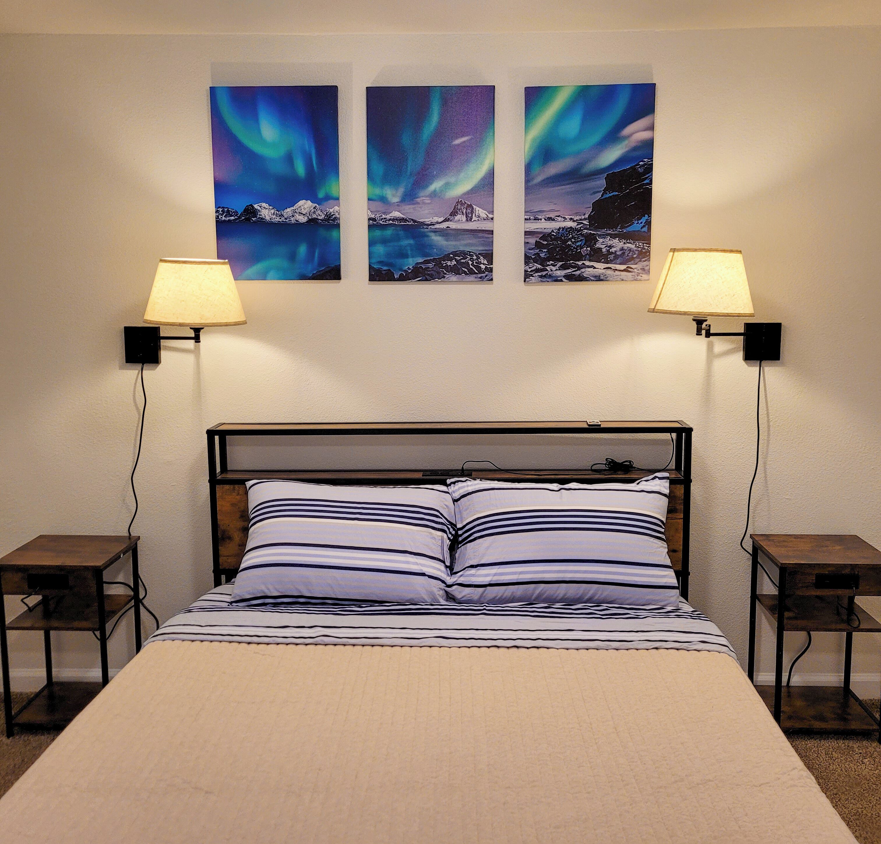 Una cama con ropa de cama a rayas, dos mesitas de noche y tres lámparas de pared.