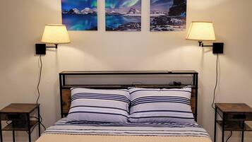 Una cama con ropa de cama a rayas, dos mesitas de noche y tres lámparas de pared.