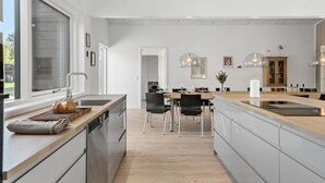 Een moderne keuken met een centraal eiland, roestvrijstalen apparatuur en een eetgedeelte met een houten tafel en stoelen.